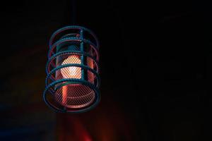 Loft pendant lamp with red blue glow in steel rebar shade, wooden interior background, copy space photo