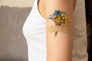 flor azul y amarilla debajo del parche en la mano de una mujer. el concepto de vacunación y tratamiento en ucrania foto