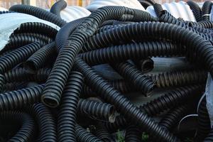 Rolled up pile of twisted, high pressure flexible black rubber pvc plastic hoses, construction material and equipment at building site. Conduit, goffred tubing pipes. Drain sewage tube pipeline photo