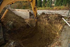 una excavadora de carreteras draga el agujero cerca de la casa familiar foto
