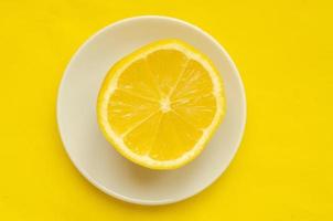 Top view, one slice of lemon on a white saucer on a yellow background photo