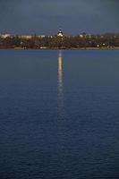 The golden dome of the Orthodox Church, standing on the banks of the river, is reflected on the surface of the water. Golden walkway from the church dome on the surface of the river. photo