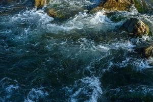 flujo, por un río tormentoso entre las rocas en el parque de otoño en un día cálido foto