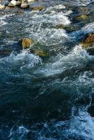 flujo, por un río tormentoso entre las rocas en el parque de otoño en un día cálido foto