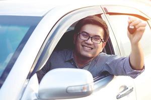 hombre de negocios mano sujetando las llaves del coche delante con un coche nuevo en el fondo. estacionamiento en frente de la casa. concepto de transporte. deje espacio de copia para escribir mensajes de texto. foto