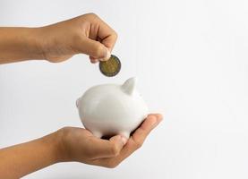 A piggy bank in hand and is putting coins in a piggy bank with copy space on white background. photo