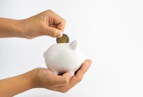 A piggy bank in hand and is putting coins in a piggy bank with copy space on white background. photo