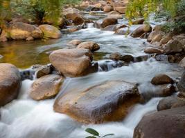 una toma de larga exposición de un pequeño arroyo que fluye a través de una roca marrón. y hay árboles verdes como telón de fondo. es un enfoque específico. foto