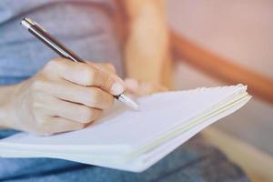 close up hand young woman are sitting on a chair. using pen writing Record Lecture note pad into the book on the table. photo