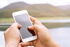 joven usa camisa a cuadros. cierre la mano usando el teléfono celular durante el descanso en el sofá. sentado viendo un mensaje en un teléfono inteligente móvil durante el descanso, relájese. enfoque suave. foto