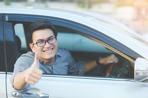 Portrait of happy smiling Young asian man traveler on the road showing thumbs up while driving in his car. photo