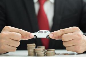 Business man in suit and close up hand holding model of toy car  on over a lot money of stacked coins - insurance, loan and buying car finance concept. buy and installments down payment  a car photo