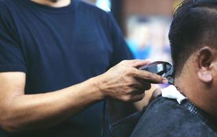 corte de pelo de hombre de persona que se afeita el cabello con estilo, con cortapelos de peluquero peluquero con las manos en la barbería. tono vintage de relleno y enfoque suave selectivo. foto