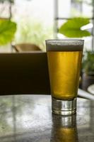 glass of beer on a terrazzo table, two yellow chairs in the background, retro table, window with natural light photo