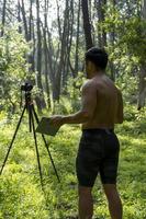 Mature middle-aged athlete man standing in stand position in sporty clothes on fitness mat, watching video training tutorial online, vlogging photo