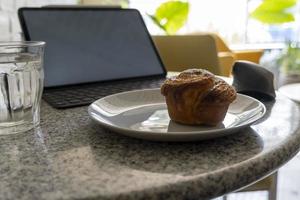 pancake or cupcake on ceramic plate, terrazzo table, tablet in the back. Enjoying sweet bread while working photo