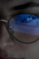 young woman, watching the stock market at night, the same market is seen in the reflection of her glasses photo