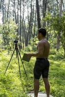 Mature middle-aged athlete man standing in stand position in sporty clothes on fitness mat, watching video training tutorial online, vlogging photo