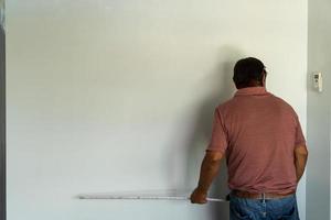 el hombre mayor mide la pared con cinta métrica reparando el apartamento. marido maduro redecorar la casa foto