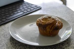 pancake or cupcake on ceramic plate, terrazzo table, tablet in the back. Enjoying sweet bread while working photo