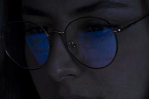 young woman, watching the stock market at night, the same market is seen in the reflection of her glasses photo