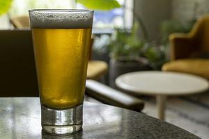 glass of beer on a terrazzo table, two yellow chairs in the background, retro table, window with natural light photo