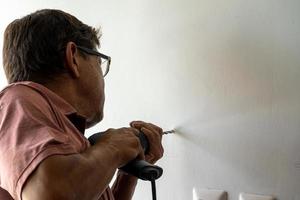 hombre latino de unos 50 años, perforando una pared con un taladro, pared blanca foto