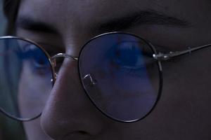 mujer joven, mirando el mercado de valores por la noche, el mismo mercado se ve en el reflejo de sus gafas foto