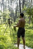 Mature middle-aged athlete man standing in stand position in sporty clothes on fitness mat, watching video training tutorial online, vlogging photo