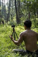 Millennial guy meditating with trainer online via tablet ipad connection, in the forest, broadcasting online your class and instructions, mexico photo