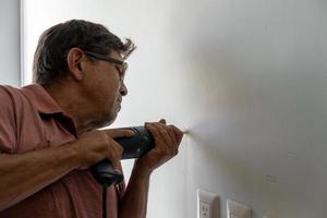 latino man using a power drill to drill holes in the wall to hang a new television, drilling holes in the wall, mexican, hispanic photo