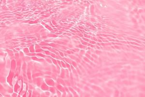 desenfoque borroso transparente color rosa claro agua tranquila textura superficial con salpicaduras, burbujas. fondo de ondulación de agua rosa brillante. superficie del agua en la piscina. agua de burbujas rosadas que brilla. foto