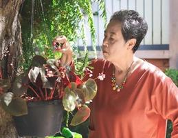 happy and healthy Asian senior woman taking care of plants outdoors, triming  dry leaves. photo