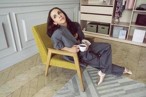 ballerina in a gray striped suit with a cup of coffee smiling and dreaming is sitting in an armchair photo