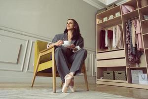 ballerina in a gray striped suit with a cup of coffee smiling and dreaming is sitting in an armchair photo