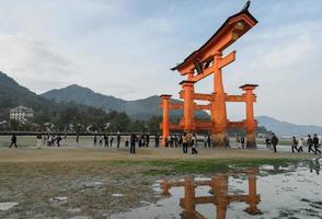 miyajima, japón, 2016 - el gran o-torii del santuario itsukushima. los turistas caminan alrededor de la famosa puerta torii flotante del santuario itsukushima en miyajima durante la marea baja en miyajima, japón foto