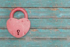 A red heart-shaped lock against a background of old blue wooden planks. photo