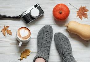 Legs of a girl in knitted socks on a wooden background next to pumpkins and autumn leaves photo