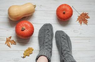 Legs of a girl in knitted socks on a wooden background next to pumpkins and autumn leaves photo