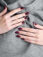 manos de una mujer joven con manicura roja oscura en las uñas foto