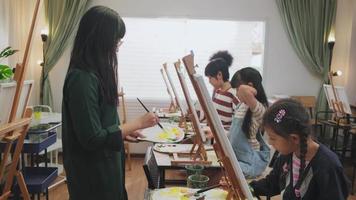 A group of multiracial kids learning with a female Asian teaches acrylic color picture painting on canvas in art classroom, creatively learning with skill at the elementary school studio education. video
