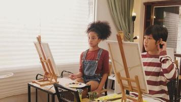 enfants en studio d'art, deux étudiants afro-américains et asiatiques apprennent avec une enseignante, peinture acrylique couleur sur toile en classe, créativité avec compétence dans l'enseignement primaire. video