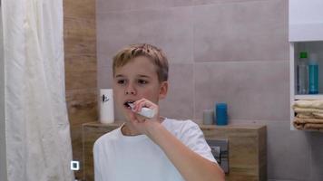 aktiva skol borstar hans tänder med en tandborste i de morgon- i de badrum. morgon- hygien förfaranden. video