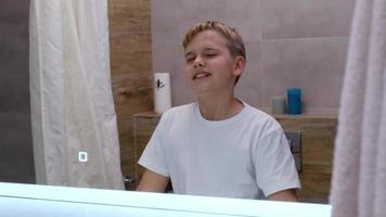 grappig vrolijk tiener zingt in de badkamer in voorkant van de spiegel in de ochtend, knipoogt Bij zijn reflectie. actief begin van de dag video