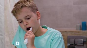 Sleepy schoolboy brushes his teeth in the bathroom in front of a mirror. Tired boy carries out morning hygiene procedures. video