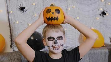 ein fröhliches kind mit einem make-up in form eines skeletts und einem kürbis auf dem kopf feiert halloween. Allerheiligen im Oktober video