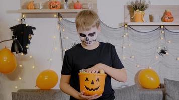 een jongen in skelet bedenken houdt een emmer van snoep. de kind viert halloween video