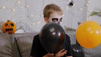 The boy is decorated as a skeleton plays with balloons celebrating Halloween at home. Child is Ready for the trick or treat holiday. video
