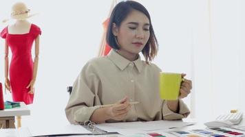 beautiful designer is drinking coffee to cure sleepiness in a tailor's shop. video