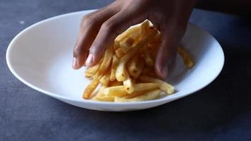 Close up of hand grabbing french fries from a white dish